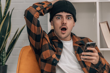 Wall Mural - young man at home with mobile phone and surprised expression