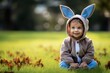 Little baby in easter bunny dress sitting and smiling on green grass, cute baby boy in costume. Easter congratulating concept with copy space.