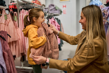 The mom shows her daughter a piece of clothing she wants to buy, pressing it against her to check the size and envisioning how it will look.