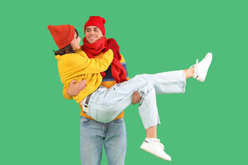 Wall Mural - Happy young couple in warm clothes having fun on green background