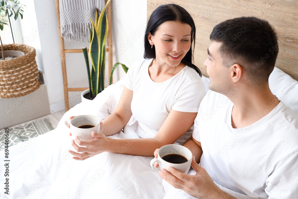 Young couple with cups of coffee in bedroom