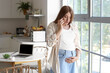 © Pixel-Shot - Young pregnant woman talking by mobile phone near window at home