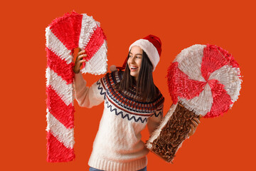 Poster - Young woman in Santa hat with candy pinatas on orange background