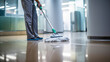 Lower body of a person in green scrubs and white shoes mopping a shiny hospital floor