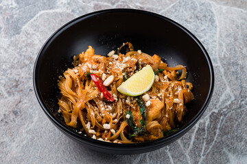 Poster - Rice noodle pad thai with chicken, onion, chilli, lime, nuts and herbs in a bowl.