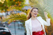 © Alliance - smiling trendy woman in pink dress and white jacket in city