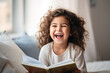 Happy little girl reading a book while sitting on the sofa at home