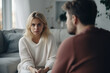 Оffended young blonde woman and man argument, сlose up husband in front and upset wife behind sit at sofa quarrel at home. Family conflict, crisis, psychological abuse, relationships concept
