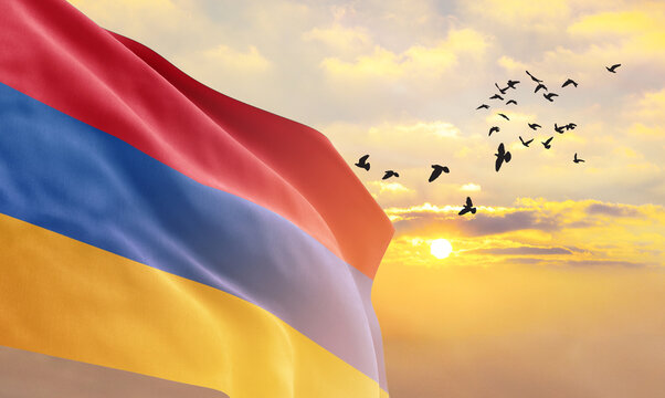Waving flag of Armenia against the background of a sunset or sunrise. Armenia flag for Independence Day. The symbol of the state on wavy fabric.