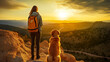 A woman and her golden retriever standing on a mountain cliff, looking at a sunset.