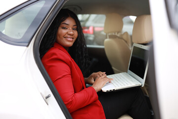 Wall Mural - beautiful african passenger in the back seat of a car with a laptop