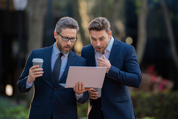 Wall Mural - Two businessman using laptop outdoor. Business men team using laptop outdoor. Businessmen looking laptop with their business success in city background. Two business teams success.