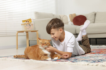 Canvas Print - Little boy petting cute ginger cat on carpet at home