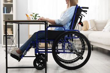 Wall Mural - Woman in wheelchair using laptop at table in home office, closeup