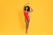 Beautiful woman in bright one-piece summer swimsuit on yellow background