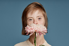 Girl Covering Mouth With Crown Daisy Against Blue Background