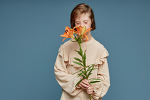 Teenage Girl Smelling Orchid Flowers Standing Against Blue Background