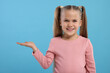 Special promotion. Little girl showing something on light blue background. Space for text