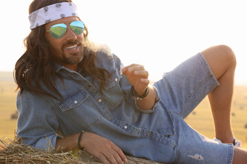 Wall Mural - Hippie man smoking joint on hay bale in field