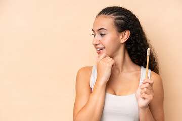 Wall Mural - Young woman brushing teeth isolated on beige background thinking an idea and looking side