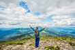 © Yevhen - Woman with backpack rise to the mountain top, raises his hands up. Girl atop a rock just off a hiking trail mountain. Success woman hiker hiking on mountain peak. Young traveler girl with backpack