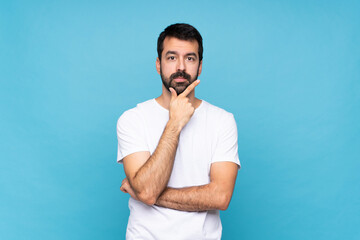 Wall Mural - Young man with beard  over isolated blue background thinking