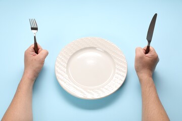 Wall Mural - Man with cutlery and empty plate at light blue table, closeup