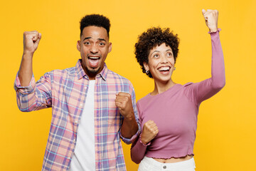 Wall Mural - Young couple two friends family man woman of African American ethnicity in purple casual clothes together do winner gesture celebrate clench fists say yes isolated on plain yellow orange background