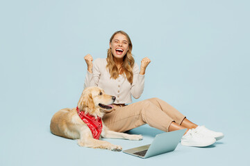 Wall Mural - Full body winner fun young owner IT woman wears casual clothes sit near her best friend retriever dog work hold use laptop pc computer isolated on plain blue background. Take care about pet concept.