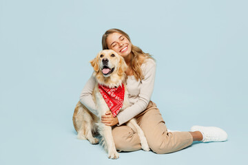 Full body young owner woman wear casual clothes sit hug cuddle embrace look at her best friend retriever dog in red bandana close eyes isolated on plain blue background. Take care about pet concept.