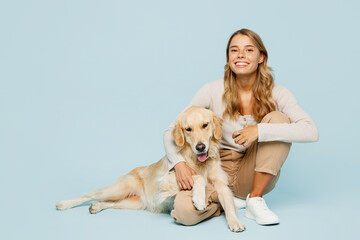 Wall Mural - Full body smiling happy young owner woman wearing casual clothes sitting hug cuddle embrace her best friend retriever dog isolated on plain light blue background studio. Take care about pet concept.