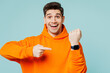 Young surprised shocked man wears orange hoody casual clothes show time point index finger on smart watch isolated on plain pastel light blue cyan color background studio portrait. Lifestyle concept.