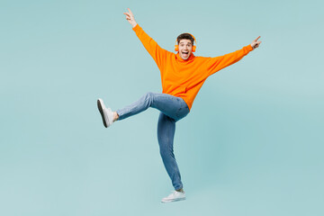 Wall Mural - Full body overjoyed excited young man wears orange hoody casual clothes listen to music in headphones spread hands dance isolated on plain pastel light blue cyan color background. Lifestyle concept.