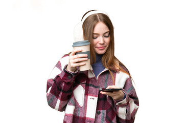 Sticker - Young pretty woman wearing winter muffs over isolated chroma key background holding coffee to take away and a mobile