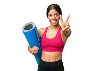 Wall Mural - Young sport African American woman going to yoga classes while holding a mat over isolated background smiling and showing victory sign