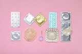 Fototapeta  - Contraceptive pills, condoms and intrauterine device on pink background, flat lay. Different birth control methods