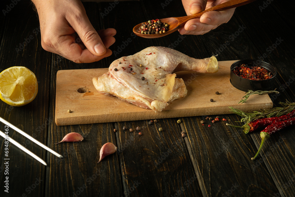 Cooking chicken leg on a kitchen board by the hands of a chef. The cook ...