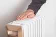 A man's hand against the background of an electric heater radiator on a white background. Concept of heating season in apartments in winter and autumn, close-up. Overheat protection