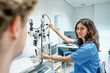 © ADDICTIVE STOCK - Happy young woman doctor standing near slit lamp biomicroscope with anonymous man in hospital