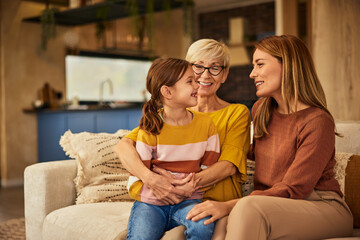 Canvas Print - Photo of three generations. A little girl sitting on her grandma's lap, smiling and looking at her mother.