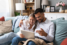 Excited Young Couple Sitting On Couch In Formal Wear With Tablet Pc, Celebrating Online Win, Great Deal Or Business Success At Home. Millennial Spouses Enjoying Big Sale In Web Store.