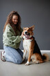 Full length portrait of curly haired young woman petting happy mixed breed dog sitting on floor in studio