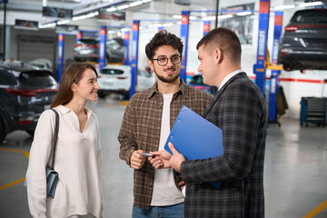 Wall Mural - Salesman giving keys of new car to young man and woman in modern dealership