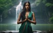 Indian woman in green saree showing namaste sign in jungles. Beautiful young female with long dark hair standing with waterfall on the background