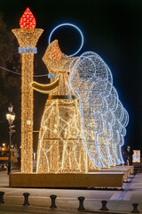 Wall Mural - Christmas lights decoration in the shape of an angel holding a torch in from of The Palace of San Telmo, In Seville, Andalusia, Spain. Selective focus with focus in the nearest angel