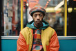 Estilo vibrante: Retrato de un apuesto hombre afroamericano con abrigo y sombrero coloridos esperando en la parada de autobús
