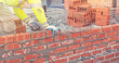 Bricklayer in safety vest and a helmet laying a brick wall using a trowel