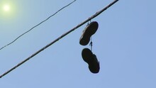 Pair Of Shoes Dangling From Telephone Wires Against Blue Sky. 4K Resolution.