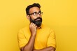 Thoughtful bearded Indian man holding hand on chin looking interested aside at copy space isolated on yellow background thinking of new job opportunities, having doubt question or deciding concept.