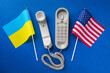 Top view of an old telephone and two flags on a blue background, concept on the theme of telephone conversations between Ukraine and America